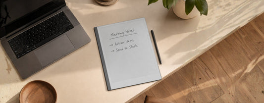 A reMarkable tablet open on a meeting notes page, placed next to a laptop on a clean desk with natural light.